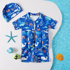 A children's full-body swim outfit laid flat on a white surface with a blue water-textured area at the right. The set includes a short-sleeve zip-front one-piece in bright blue with white anchor, whale, dolphin, crab, and turtle motifs, plus a matching blue swim cap.

