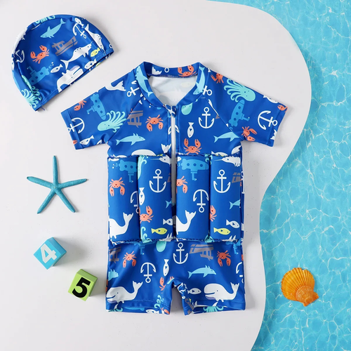 A children's full-body swim outfit laid flat on a white surface with a blue water-textured area at the right. The set includes a short-sleeve zip-front one-piece in bright blue with white anchor, whale, dolphin, crab, and turtle motifs, plus a matching blue swim cap.

