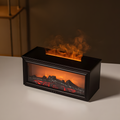 A rectangular black electric fireplace tissue box cover or decorative firebox with glowing orange flames and faux logs, shown on a tabletop in a dim interior setting.

