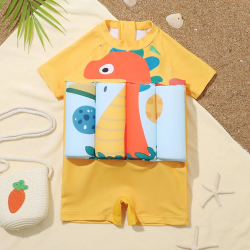 Yellow children's swimsuit with dinosaur design on a sandy background

