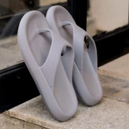 Pair of gray flip-flops on a stone surface near a glass door.

